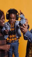 Vertical Enthusiastic father playing online games with baby boy using controller, both parents enjoying leisure time with their small kid. African american happy family play with joystick. Camera B. video