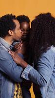 Vertical Portrait of african american family with a little child posing on camera, showing gratitude and sympathy towards each other and feeling satisfied. Happy mom and dad holding their boy. Camera B. video