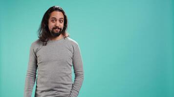 Smiling man greeting friends, happy to see them, isolated over blue studio background. Friendly person waving hand, saluting mates, being friendly, studio backdrop, camera B video