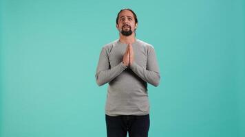 Portrait of man putting hands together in begging gesture, making wish, hoping for good news isolated over studio background. Person waiting for results, praying for positive outcome, camera A video