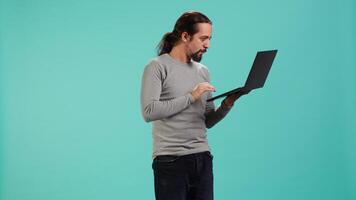 Upset man frowns while looking at laptop, dissatisfied with company profits, studio backdrop. Irked worker flabbergasted by low business income revenue, doing financial analysis on notebook, camera A video