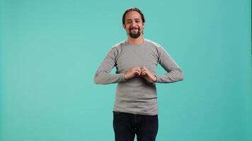 Portrait of joyful friendly man doing heart symbol shape gesture with hands. Smiling nurturing person showing love gesturing, isolated over blue studio background, camera A video