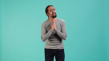 Man putting hands together in begging gesture, making wish, asking for favor from friend, isolated over studio background. Desperate person asking for something, praying and hoping, camera A video