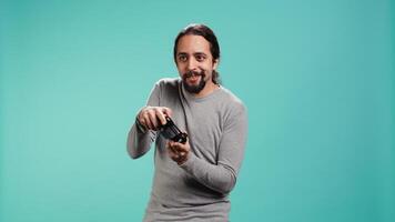Cheerful player happy after winning gaming console game, shaking fist, studio background. Portrait of man satisfied after being victorious in videogame, defeating all enemies using gamepad, camera B video