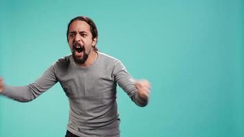 Portrait of irate man feeling outraged, yelling at friend, releasing pent up emotion, studio backdrop. Furious person full of rage screaming at mate isolated over blue studio background, camera B video