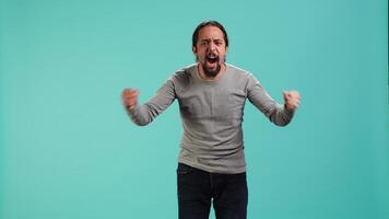 Portrait of irate man feeling outraged, yelling at friend, releasing pent up emotion, studio backdrop. Furious person full of rage screaming at mate isolated over blue studio background, camera A video