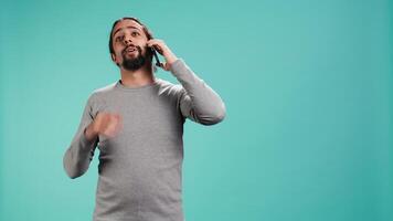 Joyous man catching up with friends in phone call using cellphone, studio background. Portrait of radiant person having conversation with mates during telephone call, camera B video