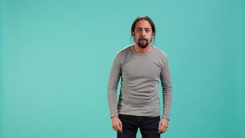 Portrait of frightened man covering his face with hands, standing isolated against studio background. Scared person with fearful facial expression suffering shock, feeling distraught, camera A video