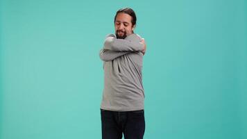 Portrait of man standing in studio, hugging himself in gesture of comfort and self love, isolated over studio background. Cheerful person doing self acceptance, embracing himself, camera A video