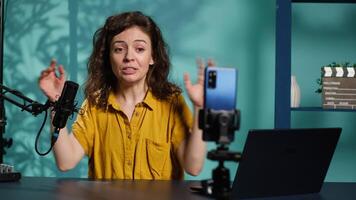 Streamer doing live broadcast on smartphone on holder, talking to audience about recent news headlines. Media star talking with viewers, presenting facts in entertaining manner, camera A video