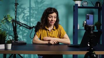 Smiling woman in studio using smartphone on phone holder to record , greeting subscribers. Happy online star hosts q and a session with viewers using cellphone, saluting fans, camera B video