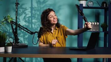 Woman using smartphone on selfie stick to capture footage, chatting with online audience. Viral content creator talking with fans, filming with high quality mobile phone, camera B video