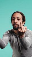 Vertical Irked man fighting with friend, doing middle finger sign gesturing, isolated over studio background. Outraged person arguing during conversation, doing obscene hand gestures, camera B video