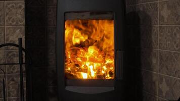 Flickering flames blaze within a sleek, modern fireplace, casting warm light against tiled walls on a chilly evening, creating a cozy atmosphere. video