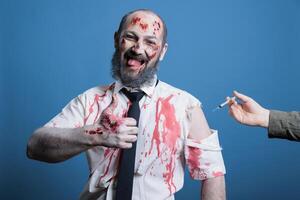 Cheerful man covered in blood and bruises receiving antidote serum after being attacked by feral animals, showing thumbs up sign. Hurt person getting remedy vaccine, studio background photo