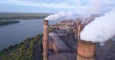 Industrial zone with a large pipe thick white smoke is poured from the factory pipe. Pollution of the environment. a pipe with smoke. Old factory near the river in Kamenskoye, Ukraine. Aerial view. video