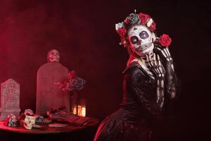 Girl in grave site at Dia de los Muertes indigenous rites of honoring the dead. Woman with rose participating in Day of the Dead celebration in honor of the deceased, red light background photo