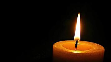 A single yellow candle is lit in the dark photo