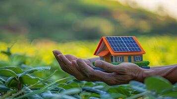 A person holding a small house in their hand with a solar panel on top photo