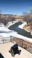 An elderly man in a wheelchair sits on a balcony overlooking a river photo