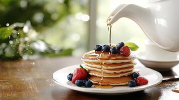 A white teapot pouring syrup over a stack of pancakes photo