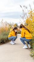 Two girls crouching down on the ground in front of a yellow bush photo
