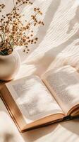 An open book and a vase of dried flowers on a white table photo