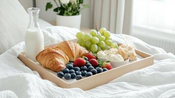 Breakfast tray with croissants, fruit and milk on bed photo