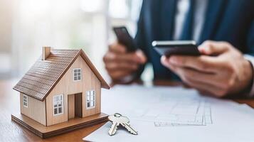 Man in business suit holding keys and looking at house model on table photo