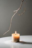 A Lit Candle on a White Surface with a Dried Branch in the Background. photo