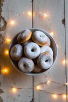 A Bowl Filled with Sweet Doughnuts Covered in Powdered Sugar and Surrounded by a String of Warm Lights on a Wooden Surface photo