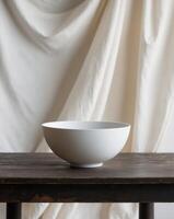 Simple white bowl placed on a wooden table with soft fabric in the background photo