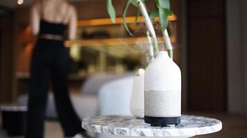 The cold steam is flowing up from the aroma diffuser on a table. Modern air humidifier device at workplace. Space for text. Person using smartphone for work and enjoying aromatherapy video
