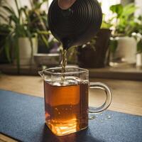 Pouring hot tea into a beautiful glass jug while surrounded by lush plants in the background photo