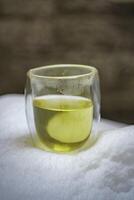 A Beautiful and Vibrant Green Beverage in a Transparent Glass Sitting on a Snowy Surface photo