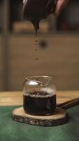Carefully pouring a rich and dark syrup into a lovely glass jar that sits on a rustic wooden slice photo