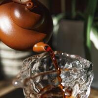 An Elegant Teapot Gently Pouring Aromatic Tea into a Clear Glass, Perfect for Enjoying photo