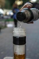 Carefully pouring a drink from a thermos into a glass bottle while enjoying the outdoors photo