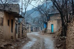 Dusty village street scene with mud houses and leafless trees. photo