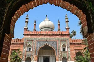 Framed view of a grand mosque with intricate details, white dome, and red brick facade under a clear blue sky. photo