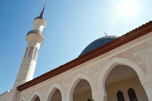 Low-angle view of a mosque's minaret and dome under a clear blue sky. photo
