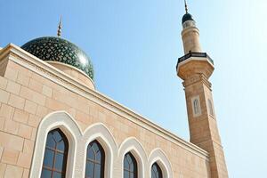 Low-angle view of a mosque with a dome and minaret under a clear blue sky. photo
