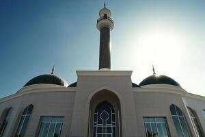 Low angle view of a mosque with two green domes and a tall minaret under a bright blue sky. photo