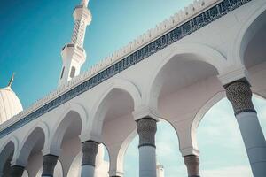 Low-angle view of white mosque architecture, intricate details, arches, minaret against blue sky. photo