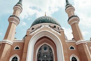 Low-angle view of a mosque's ornate facade, featuring a green dome, minarets, and intricate details. photo
