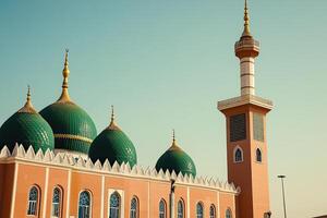 Peach mosque with green domes and minaret under a clear sky. photo