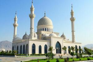 Majestic white mosque with twin minarets under a clear blue sky. photo