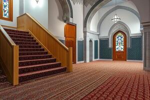 Mosque interior with staircase, stained glass, and ornate carpet. photo