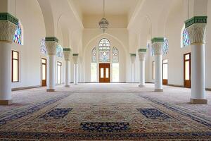 Spacious mosque interior with arched windows, columns, and ornate carpet. photo