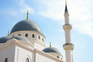 White mosque with blue domes and minaret under a bright sky. photo